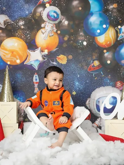 Sitting among the stars, this one-year-old astronaut is ready to explore the cosmos. The vibrant galaxy backdrop and planetary balloons create a fun and immersive setting for a milestone celebration.