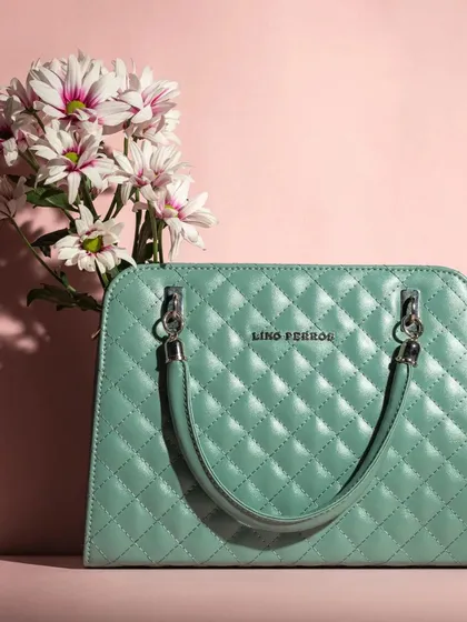 A quilted mint green handbag styled simply with a bouquet of daisies against a soft pink background. The color harmony makes this a very pleasing and commercially effective product shot.
