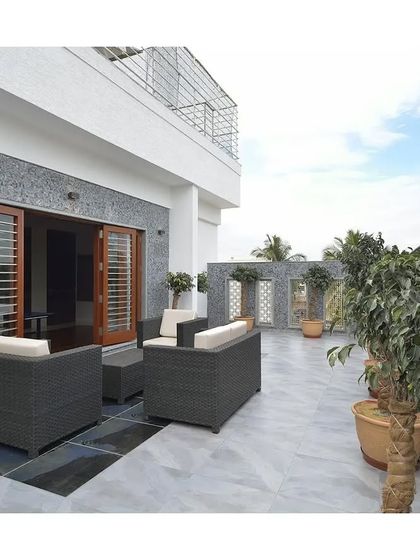 A spacious terrace with a stone-textured wall and comfortable outdoor seating. Potted trees add life and softness to the modern architectural space.