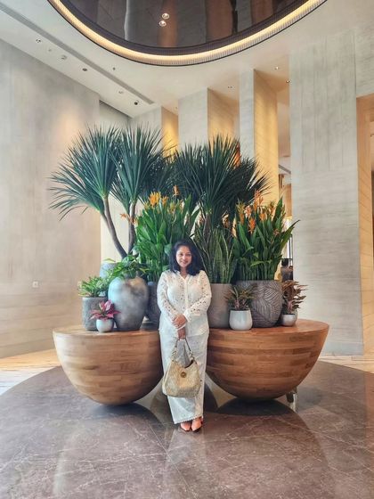 Komal, all smiles, posing with our latest plant installation. This beautiful arrangement of varied plants in wooden bowl planters is a perfect example of the lush, multi-layered look we love to create.