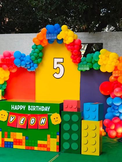 A bright and playful Lego-themed birthday party with a backdrop made of giant Lego blocks and a colorful balloon arch.