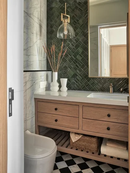 Details make the design. In this master bathroom, a custom chequerboard floor and a feature wall of jade green herringbone tiles create a bold statement. The oak-finished vanity and gold-finish sanitary fittings add a final touch of luxury, transforming a functional space into a personal spa.
