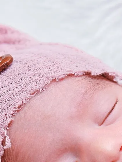 A macro shot focusing on the delicate knit of the bonnet and the baby's soft hair and closed eyelid. It's these tiny details that make each baby unique.