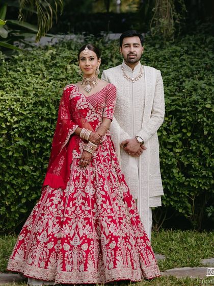 A classic couple portrait against a lush green backdrop. The bride's red lehenga and my flawless makeup application make for a stunning contrast.