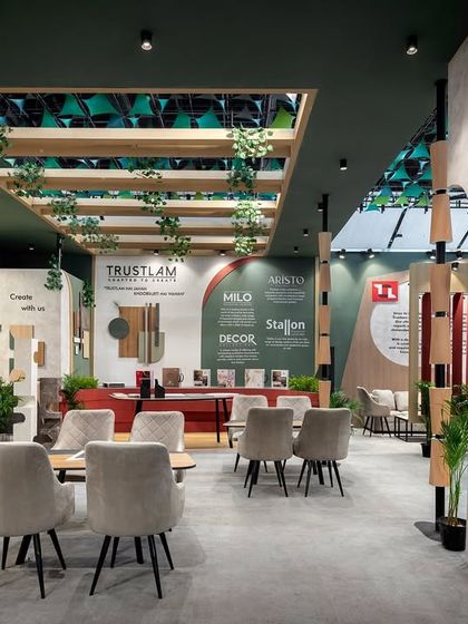 A wider perspective of the Trustlam pavilion shows the open and interactive layout. Sculptural pillars and an overhead trellis with hanging plants define the space without closing it off, encouraging visitor flow from all directions.