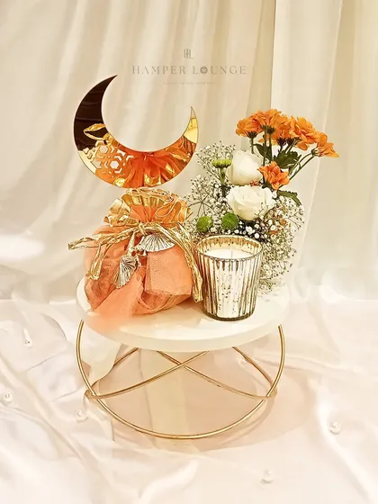 A minimal yet elegant Eid gift. This small hamper features a treat-filled potli and a scented candle, arranged on a marble-top riser with a crescent moon accent, perfect for a thoughtful gesture.
