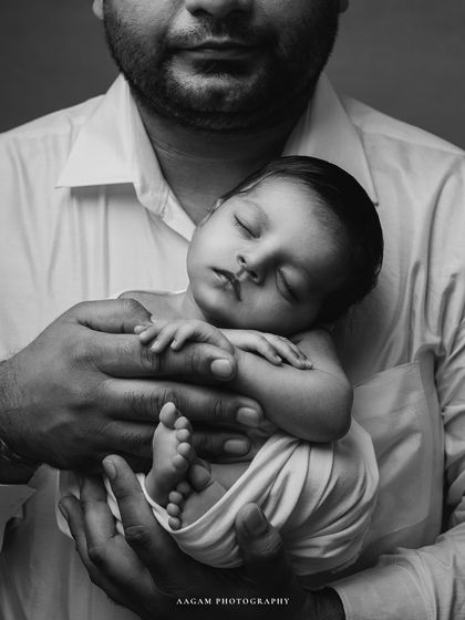 A close-up of this father-newborn moment in black and white, focusing on the tiny details of the baby and the strength of the father's hold.