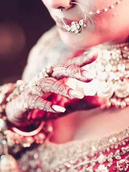 A detailed close-up of the bride's hands, focusing on her henna, nails, and the stunning coin-detail necklace.