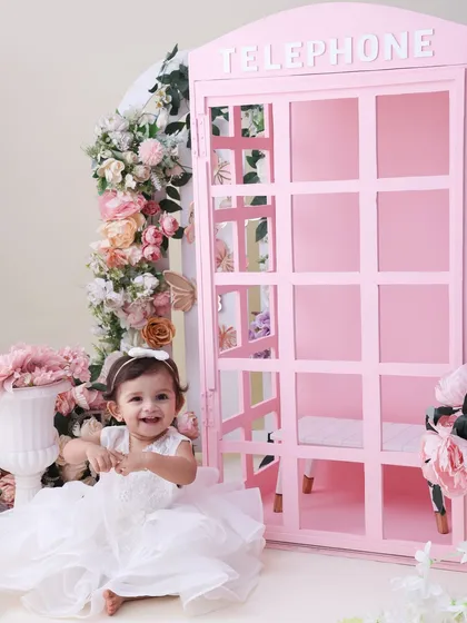 A princess in her floral wonderland. This shot captures the full view of our pink telephone booth setup, showing how the flowers and props come together to create a truly enchanting scene.