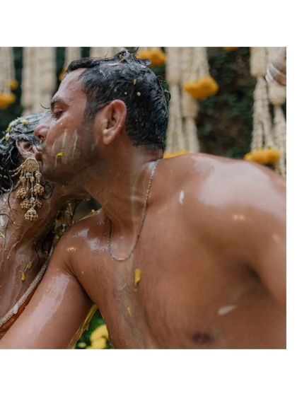 An intimate kiss shared between the couple amidst the messy, yellow-stained celebration of their Haldi.