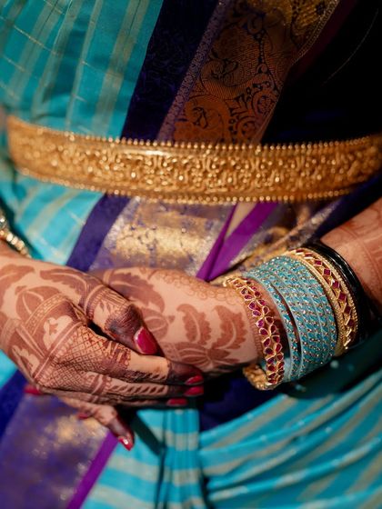 A close-up view of a rich, dark henna stain on the hands. The design features delicate leaf patterns that complement the client's beautiful silk saree and gold vaddanam.