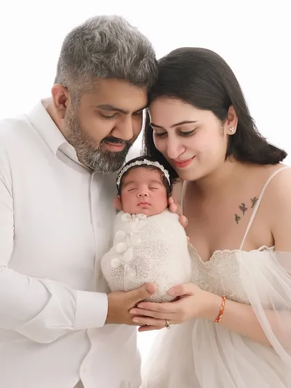 The same couple from our maternity gallery now holds their newborn daughter. Dressed in white against a clean background, this portrait beautifully continues their family's story, from anticipation to arrival.