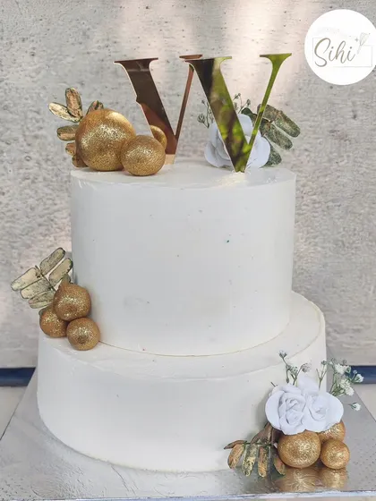 A stunningly simple two-tier white engagement cake. The clean lines are accented with clusters of gold baubles, delicate sugar flowers, and a modern initial topper for a chic and timeless look.