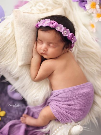 A sleeping newborn rests on a soft fur pillow, wrapped in a purple blanket. This simple and classic pose highlights the baby's peaceful features.