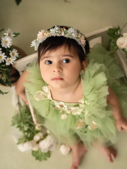 An overhead shot of a baby girl in a green floral dress, looking up at the camera with wide, curious eyes.