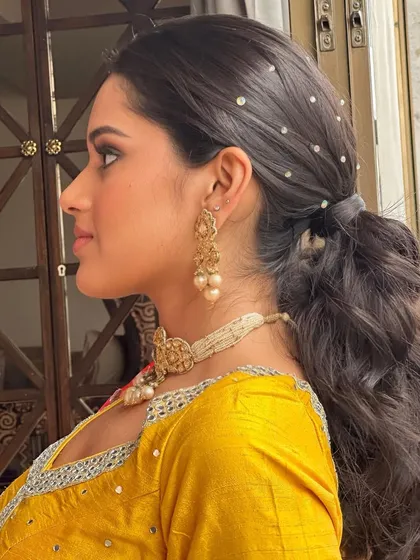 A detailed side profile of this pearl-adorned ponytail. The combination of voluminous curls and delicate pearls creates a look that is both playful and elegant, perfect for a Haldi ceremony.