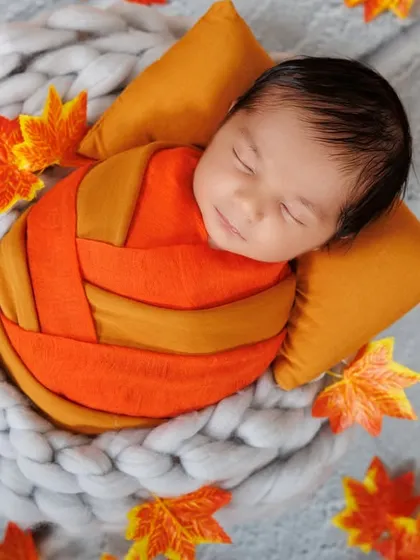 A sweet smile from a sleeping newborn, swaddled in orange and surrounded by autumn leaves. Capturing these fleeting smiles is my specialty.