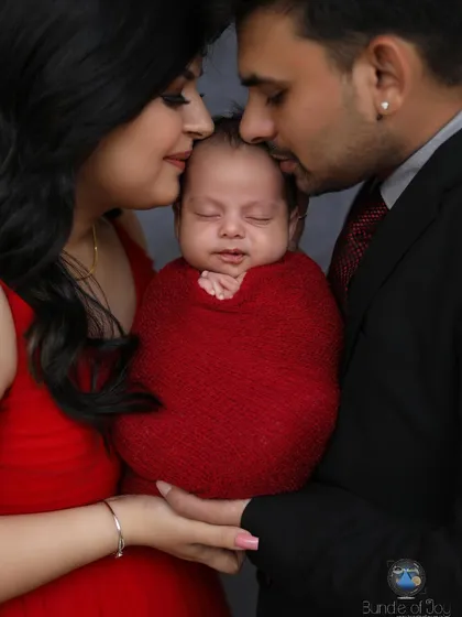 A beautiful pose showing both parents gently holding and kissing their swaddled newborn, creating a circle of love and protection around the baby.