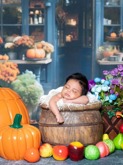 A newborn sleeping peacefully in a barrel at the market, surrounded by pumpkins and fruits.