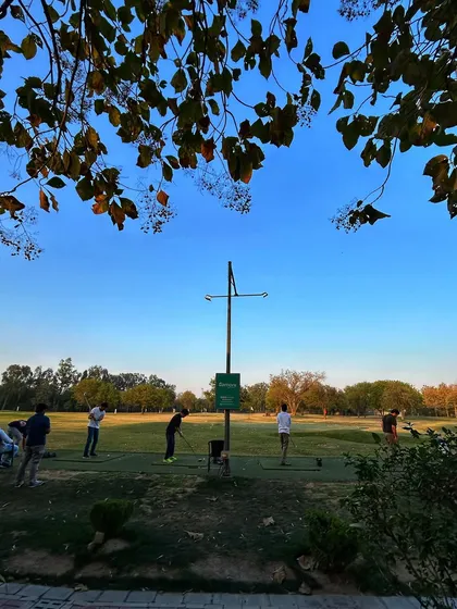 A beautiful view of the range framed by trees, with golfers enjoying the clear blue sky.