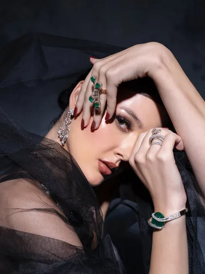 A moody and artistic shot from a jewellery editorial. The dark, sheer fabric creates a beautiful contrast with the sparkling emerald and diamond jewellery, resulting in a dramatic and high-fashion image.