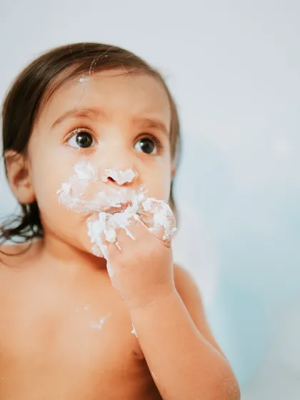 A moment of pause, looking up with a mouth full of cake. The simple background keeps all the attention on his adorable face.