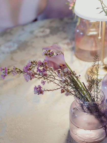A detail shot of the delicate pink and purple flowers in a glass vase, illuminated by a table lamp.