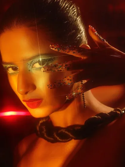 A creative and glamorous look with glitter accents around the eyes, captured with dramatic red lighting.