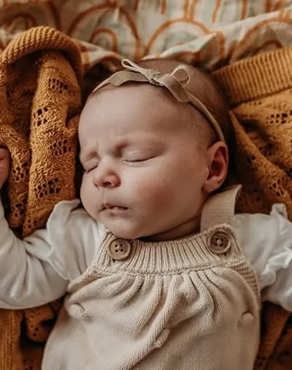 An adorable sleeping newborn with a bow headband. This overhead shot highlights the baby's peaceful expression and cute outfit.