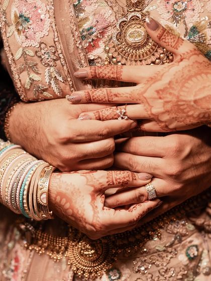 A detailed close-up shot of the couple's hands, showcasing the bride's intricate henna and their beautiful engagement rings.