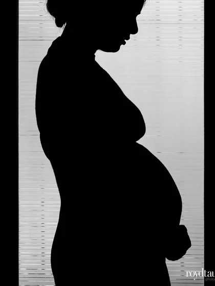A classic maternity silhouette. This powerful black and white image beautifully captures the shape of the baby bump against a softly lit background, creating a timeless and artistic pregnancy photo.
