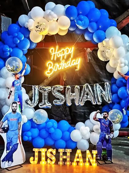 A cricket-themed birthday party for a true fan! This setup features a blue and white balloon ring, cutouts of star players like Virat Kohli, and the birthday boy's name in both marquee and foil letters.