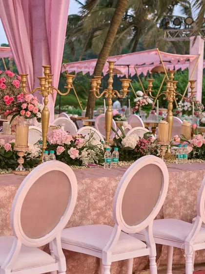 The dining setup for the beach wedding, featuring long tables adorned with golden candelabras and continuous floral runners. The design balances elegance with the relaxed beach atmosphere.