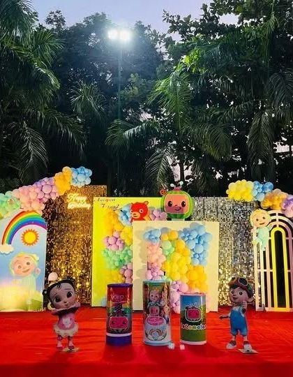 A fantastic Cocomelon stage for a second birthday, featuring a large balloon number '2', character figurines, and a colorful backdrop with rainbows and clouds.