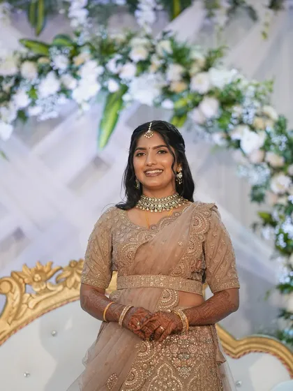 A full-length shot of this bride's reception look. The makeup is glamorous yet subtle, ensuring it photographs well against the beautiful floral backdrop without overpowering her natural features.