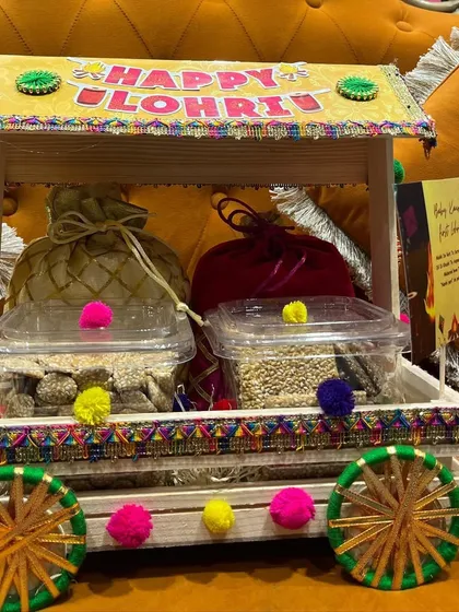 A close-up of a single Lohri favor, showing the detail of the cart and the packaged sweets like gajak and til.