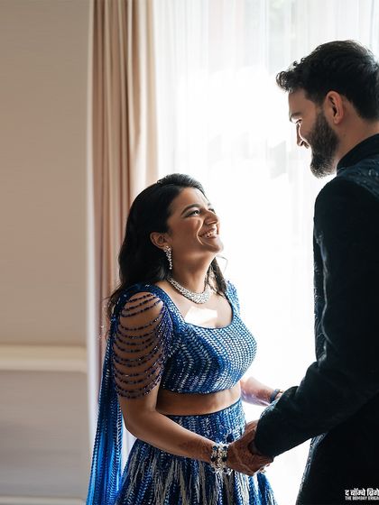A candid moment of laughter. The bride's unique blue lehenga with its beaded shoulder detail is a perfect example of how we find pieces that reflect our client's personality.