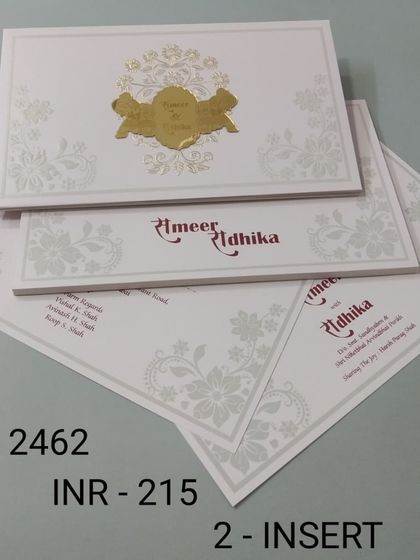 A clean and simple white invitation with a central gold foil emblem. The design includes inserts with a touch of red for the names, adding a pop of color.