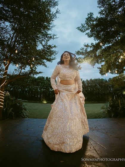 A bride laughing and running in her beautiful lehenga, captured in an outdoor setting with twinkling lights. A moment of pure, carefree happiness.