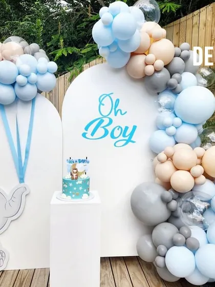 An adorable "Oh Boy" baby shower setup featuring a cute elephant cutout. The balloon arch in shades of blue, grey, and beige complements the theme perfectly, and a pedestal is included for the cake.