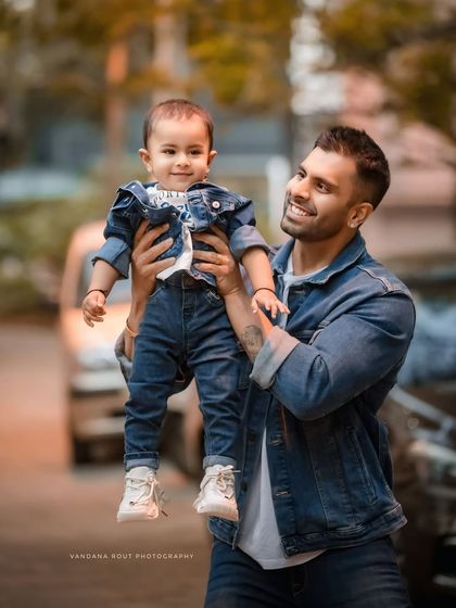 A father joyfully lifts his son, both dressed in matching denim jackets. This dynamic and happy outdoor shot is a perfect example of a candid father-son moment.