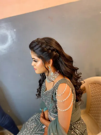 A beautiful reception look featuring a half-updo with a small braid detail and soft waves. The sparkling shoulder accessory on the blouse adds to the overall glamour.