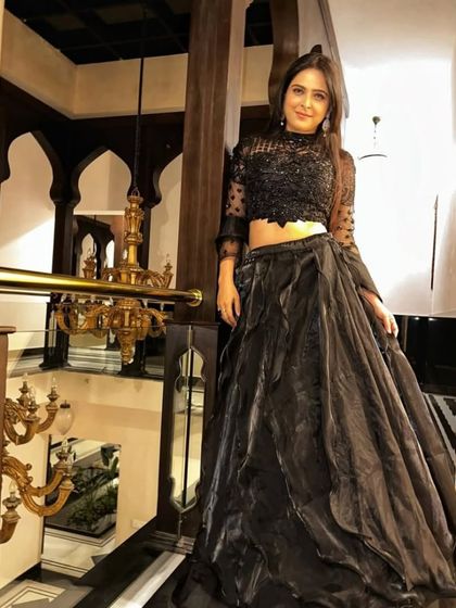 Posed on a balcony, this shot shows the modern elegance of the black lehenga gown. The embroidered crop top with sheer sleeves is both chic and sophisticated.