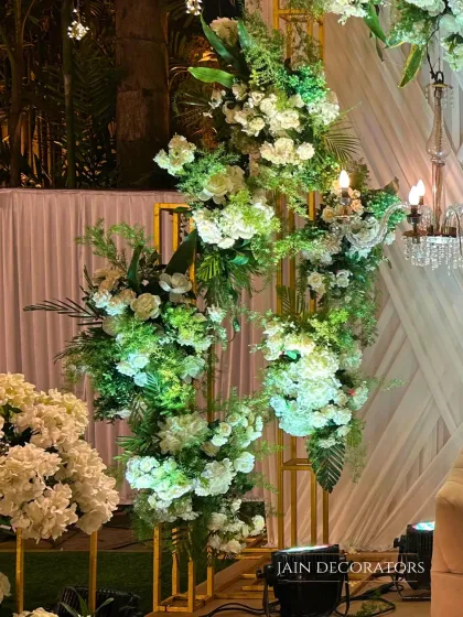 A close-up of a modern floral structure. White flowers and lush greenery are artfully arranged on a golden geometric frame, creating a piece that is both a floral arrangement and a sculpture.