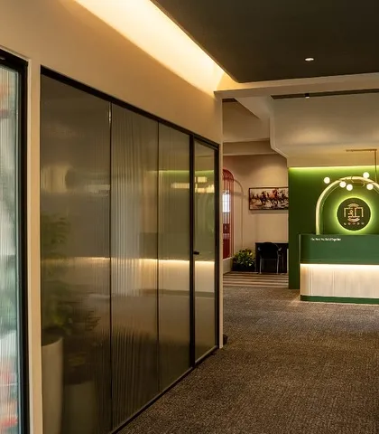 A view down the main office corridor, with fluted glass partitions for private cabins. This design choice ensures privacy while allowing light to flow through the space, maintaining a sense of openness.