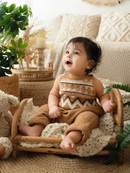A baby sits happily in a miniature cane bed in my boho-themed studio. This sitter session setup is perfect for capturing 6-month-old baby photoshoots.