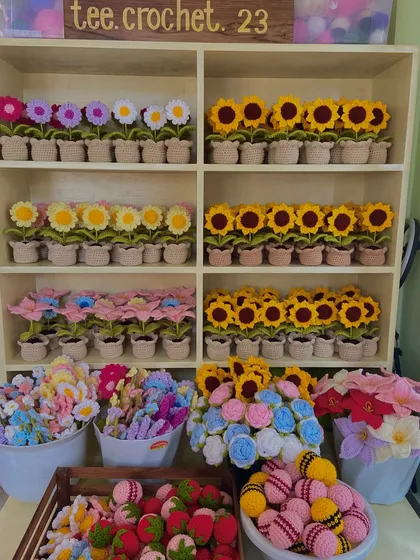 A wide shot of my workspace, showing shelves of potted flowers and buckets filled with stems and amigurumi.