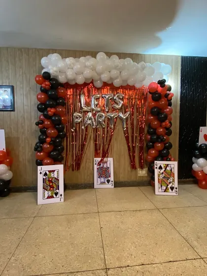 I can create fun, themed party setups like this casino or card party decoration. This design includes balloon pillars, a red tinsel curtain backdrop, 'LET'S PARTY' foil balloons, and large playing card props to complete the look.