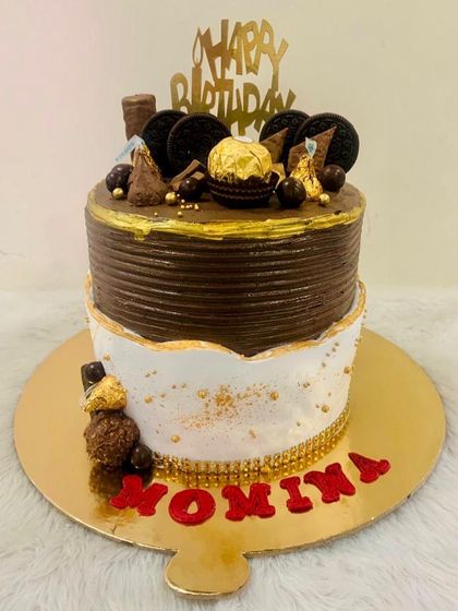 A stylish two-toned cake with a chocolate top tier and a white bottom tier, decorated with Oreos and Ferrero Rocher.