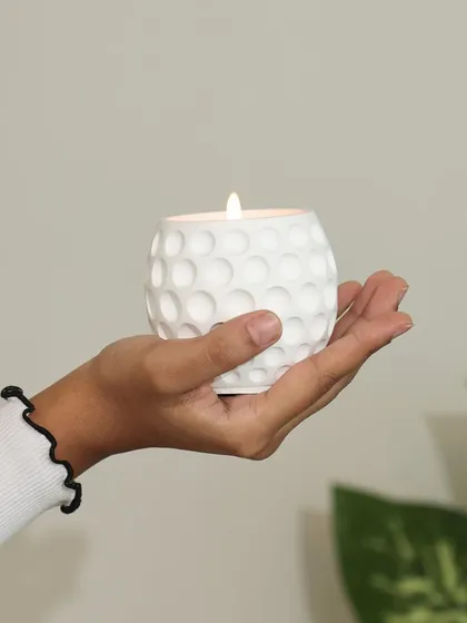 A hand holding our white scented candle with a golf ball texture. This piece is part of our minimal collection, designed to bring a touch of modern elegance and calm to your space.